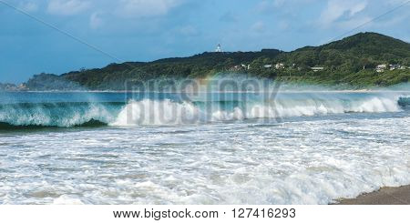 Byron Bay beach and waves in New South Wales, Australia with Cape Byron lighthouse in the background.