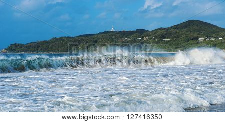 Byron Bay beach and waves in New South Wales, Australia with Cape Byron lighthouse in the background.