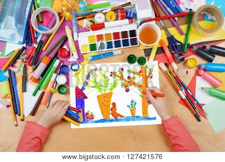 child drawing rabbit with carrot on kitchengarden near house, top view hands with pencil painting picture on paper, artwork workplace