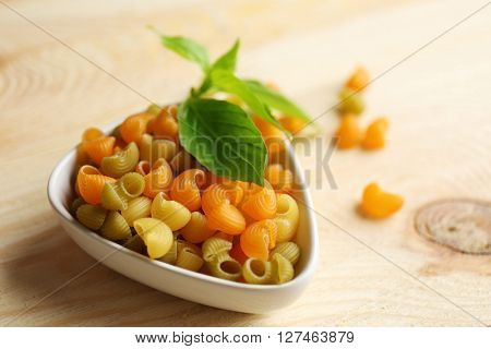 Dry multicolored gomiti pasta in white bowl on wooden table