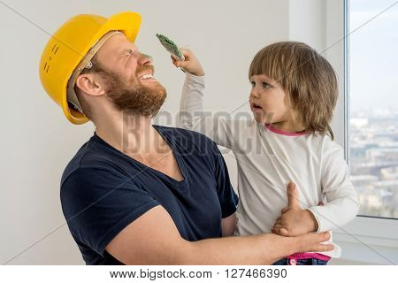 happy family, construction worker in helmet and small child with paint brush