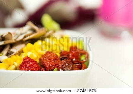 Closeup delicate fresh presentation of salad in white bowl with colourful vegetables such as mushrooms, corn and sundried omatoes.