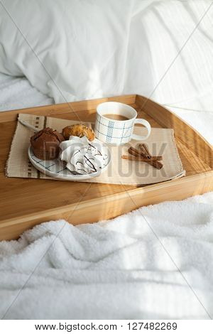 Sweet breakfast in bed served on tray with coffee and cupcakes. Sunny morning.