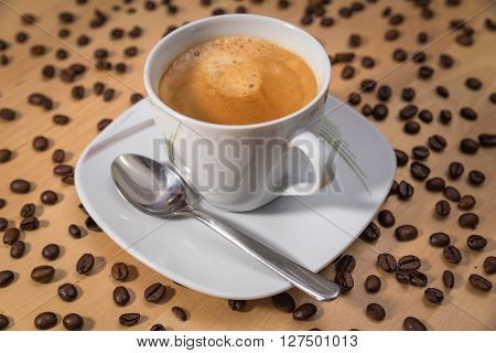 A cup of coffee with saucer and spoon ist standing on a table with many coffee beans.