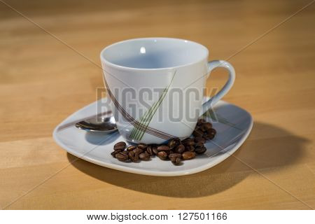 An empty cup on a saucer with a spoon is standing on a table. On the saucer are lying some coffee beans.