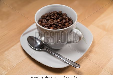 A cup filld with coffee beans ist standing on a saucer with a spoon.