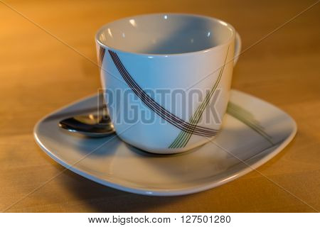 An empty cup on a saucer with a spoon is standing on a table.