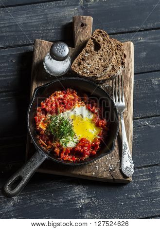 Shakshouka eggs in vintage pan on rustic wooden cutting board on a dark background. Healthy delicious breakfast or snack