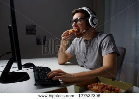 technology, gaming, entertainment, let's play and people concept - young man in headset with pc computer eating pizza while playing game at home and streaming playthrough or walkthrough video