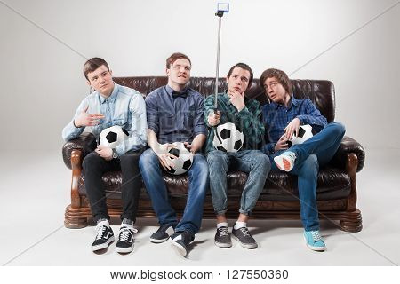 A portrait of a four guys with balls doing selfie on the couch on gray background