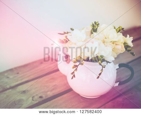 Lovely fresh bouquet of white summer roses and freesias in vintage enamel tea pot on an old brown wooden board. Retro style interior decoration with copy space.