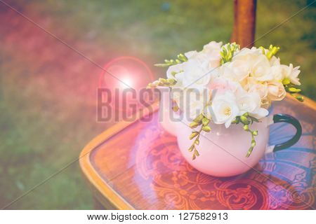 Summer wedding party festive decor, lovely fresh bouquet of white summer roses and freesias in vintage enamel tea pot on an old brown wooden chair. Retro style outdoor decoration, grass background.
