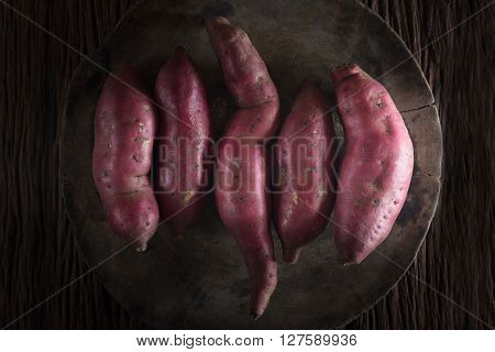 Raw sweet potatoes on wooden background.(dark style)