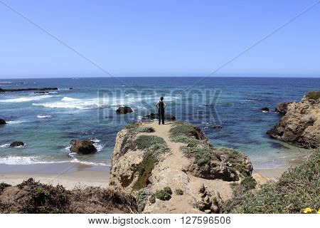 A person standing on a cliff overlooking the Pacific Ocean.