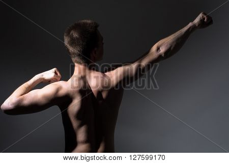 Muscular man shows back. Athletic man on a dark background