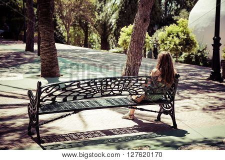 Beautiful young woman with long hair sitting on a bench in a city park