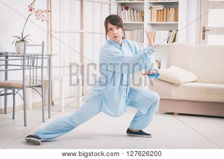 Beautiful woman doing qi gong tai chi exercise or reiki wearing professional, original Chinese clothes at home