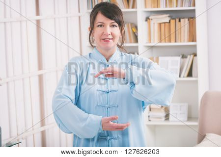 Beautiful woman doing qi gong tai chi exercise or reiki wearing professional, original Chinese clothes at home