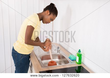 Woman Using Plunger In Sink