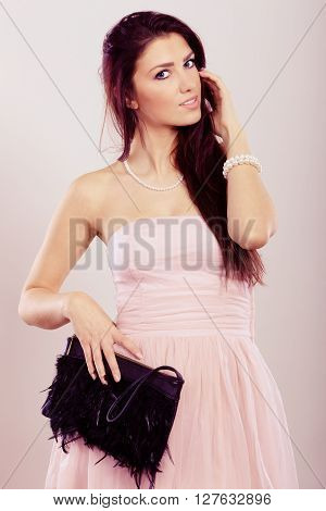 Beauty fashion and elegant people concept - young brunette slim woman in bright strapless dress holds black clutch bag