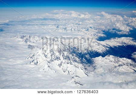 Snow covered mountains and rocky peaks in the French Alps, over blue sky. View from airplane