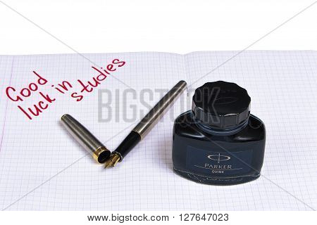 Silver with gold nib fountain pen, and a tube of blue-black ink on the background notebook with a signature.