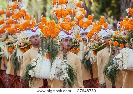DENPASAR BALI ISLAND INDONESIA - JUNE 13 2015: Group of beautiful young men in traditional Balinese people costumes carry religious offering for hindu ceremony on parade at art and culture festival