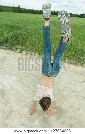 Handstand of teenage boy on dirt road at green farm field background outdoors