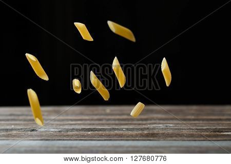 Falling penne pasta. Flying yellow raw macaroni over black background.