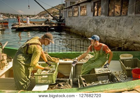 BALAKLAVA, CRIMEA, UKRAINE - JULY 1: Two young fishermen sort the catch in crates on fishing boat July 30, 2011 in Balaklava, Ukraine. Fishing is one of the main sources of income in this coastal town