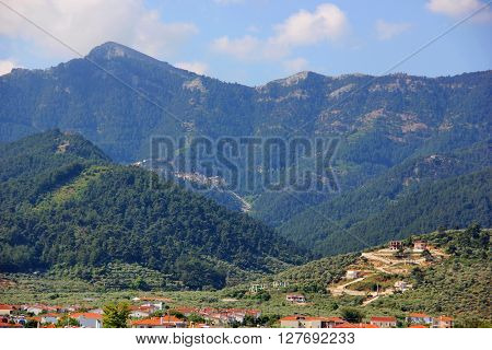 beautiful mountain range, mountains of different heights, covered with forests, greenery, village, blue sky with clouds