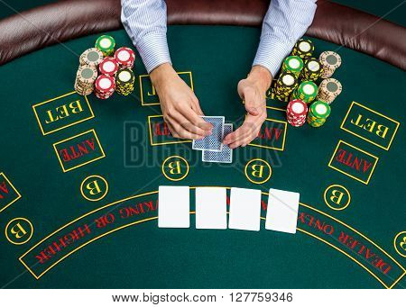 Close up of poker player with playing cards and chips at green casino table, view from above.