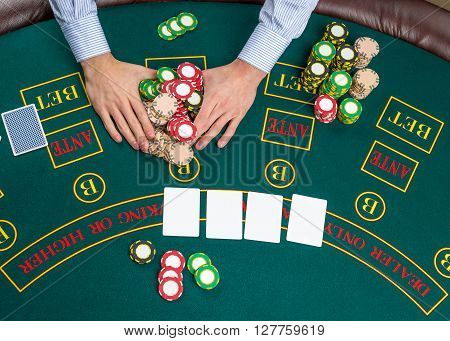 Close up of poker player with playing cards and chips at green casino table, view from above.