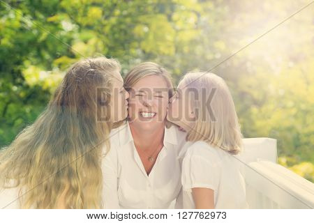 Front view of mother receiving kisses from her daughters while outside on outdoor patio. Haze light effect applied to image.