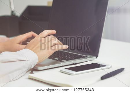 Businessperson using laptop with blank screen at white office desk. Mock up