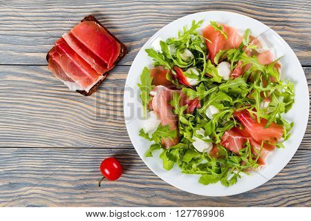 Arugula prosciutto mozzarella salad on a white dish sadwich with ham on a wooden table top view