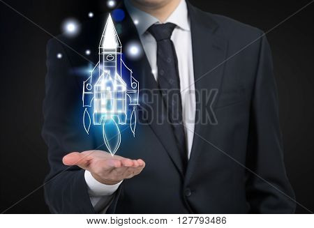 Start up concept with businessperson holding digital rocket on dark background