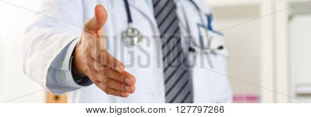 Male medicine doctor offering hand to shake in office closeup. Welcoming friend introduction or thanks gesture. Tests advertisement concept. Physician ready to examine patient. Letterbox view