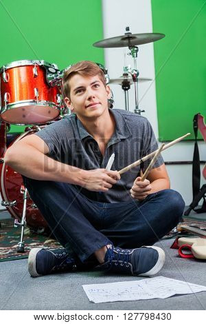 Thoughtful Professional Holding Drumsticks While Sitting On Floo