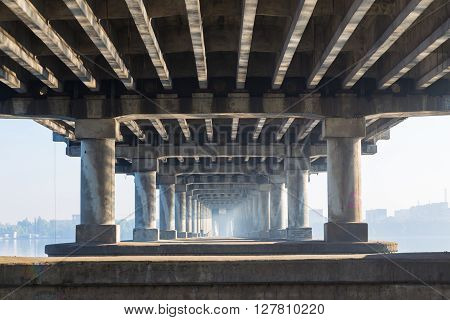 Under the bridge. Structure and architecture of the bridge in perspective illuminated by sun