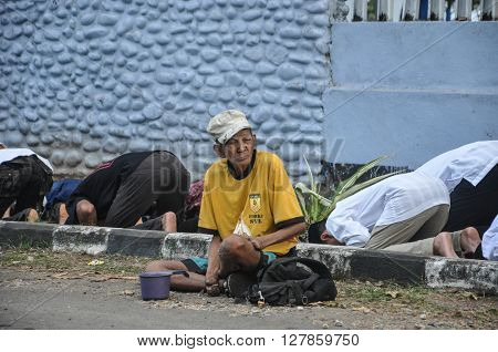 MAKASSAR, INDONESIA - CIRCA SEPTEMBER 2015: A beggar sits on the road beside the muslim devotees who performing prayer.