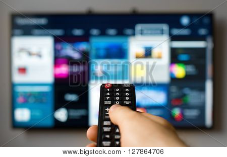 Male hand holding TV remote control against SmartTV operating system
