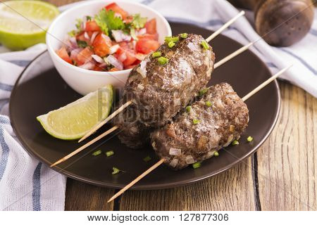 Grilled kebabs with vegetable salad and seasonings over wooden table