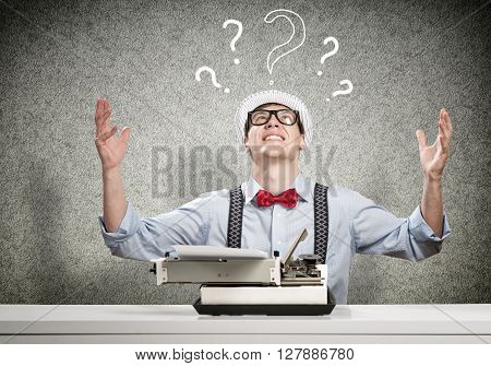 Young guy writer in hat and glasses using typing machine