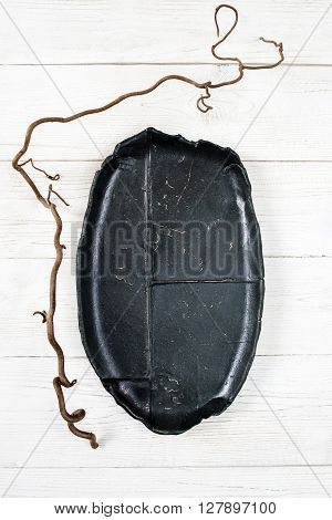 Top view empty black oval plate on rustic wooden table. Ceramic creative black plate on white wooden background with free space. Flat lay of handmade black dish on white wooden table.
