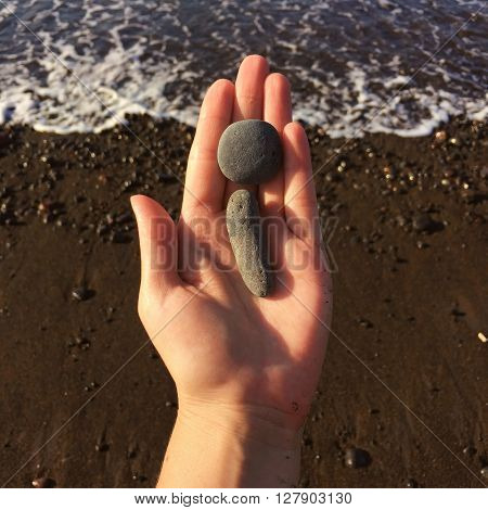 Woman hand holding small stones in hand near blue sea on a beach background