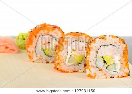 Closeup California maki sushi with masago on the wooden plate. Roll made of crab meat, avocado, cucumber and masago. Shallow depth of field.