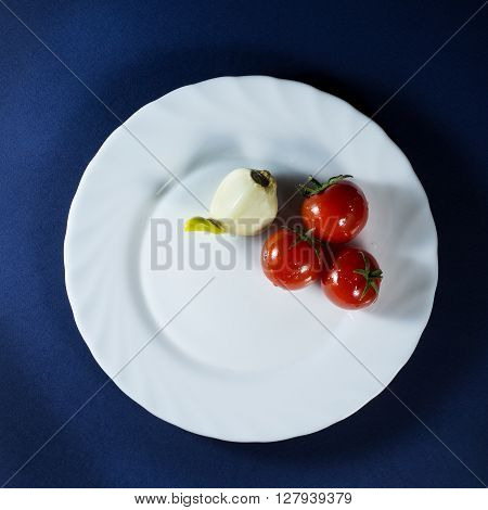 Tomatoes and clove of garlic in white plate on a dark blue background