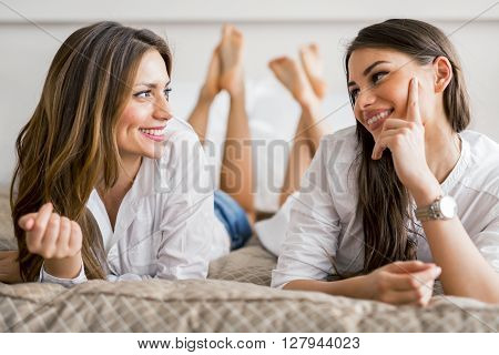 Two beautiful girls talking and smiling while lying on a luxorious bed