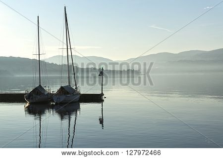 two boats in the harbor on a calm lake and the horizon mists of winter